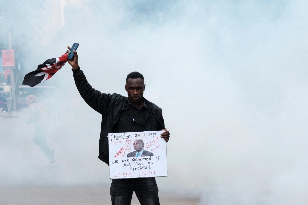 Un manifestante sostiene una pancarta y una bandera de Kenia mientras una nube de gases lacrimógenos lo rodea durante una protesta antigubernamental en Nairobi el 16 de julio de 2024. 