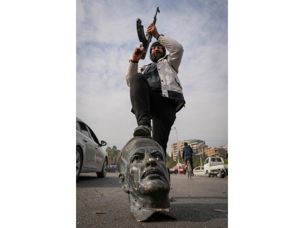 Combatiente celebra en Damasco sobre los restos de una estatua de Hafez al Assad, padre del derrocado presidente sirio Bashar al Assad.