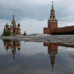 La Torre Spasskaya del Kremlin, al centro, y la Catedral de San Basilio reflejadas en el agua de lluvia en la Plaza Roja de Moscú.