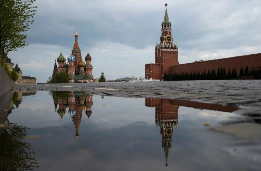 La Torre Spasskaya del Kremlin, al centro, y la Catedral de San Basilio reflejadas en el agua de lluvia en la Plaza Roja de Moscú.