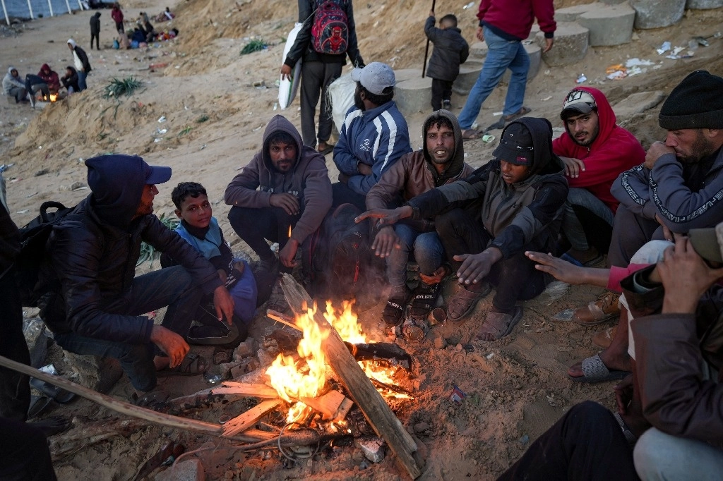 Palestinos se resguardan del frío mientras esperan que se despeje el camino para volver a casa en el noreste de la franja de Gaza.