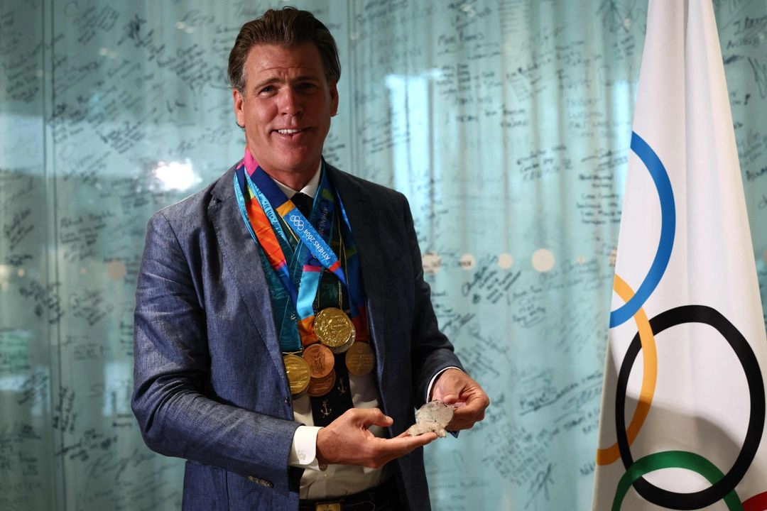 El nadador estadunidense Gary Hall Jr. (izq.) sostiene una de las medallas originales mientras el presidente del COI, Thomas Bach, le entrega réplicas de sus medallas olímpicas durante una ceremonia, en la Casa Olímpica en Lausana el 5 de mayo de 2025