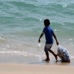 Menor recolecta envases de aluminio en una playa en imagen de archivo.