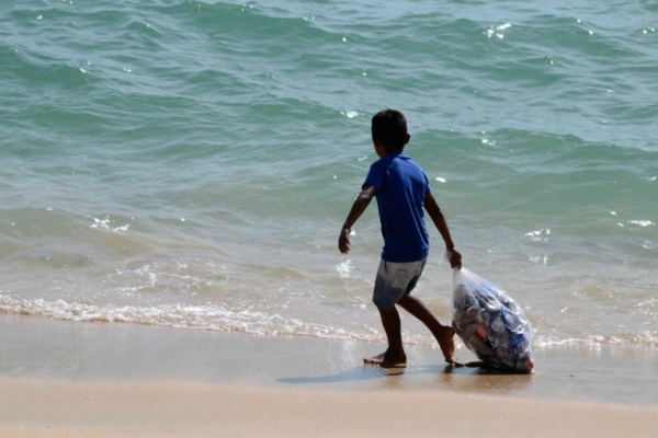 Menor recolecta envases de aluminio en una playa en imagen de archivo.