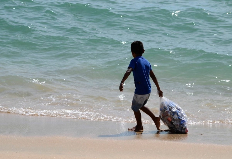 Menor recolecta envases de aluminio en una playa en imagen de archivo.