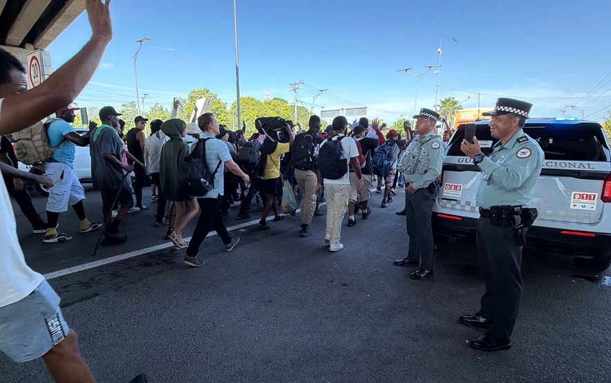La caravana "De la mano de Dios" es conformada por unos 200 migrantes, en su mayoría originarios de Cuba, Venezuela, Haití, Ecuador, Honduras y El Salvador; en la imagen, el contingente es visto pasar por elementos de la Guardia Nacional en Chiapas. 