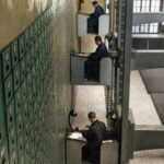 La fotografía parece de una película de ciencia ficción: tres funcionarios aparecen sentados en una especie de cabinas que son una extraña mezcla de ascensor y escritorio de trabajo.