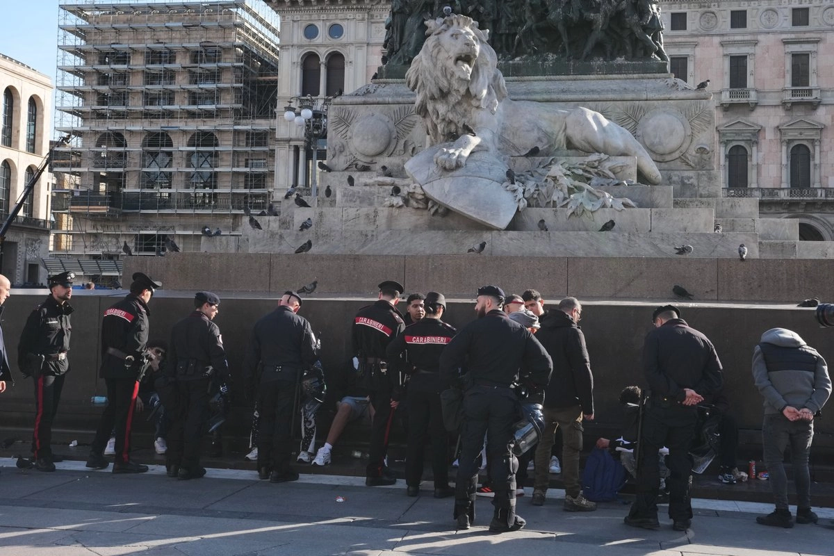 Agentes de los Carabineros conversan con personas en la plaza del Duomo, en Milán (Italia), un día después de que manifestantes violentos se enfrentaran a la policía, saquearan tiendas y prendieran fuego a propiedades.